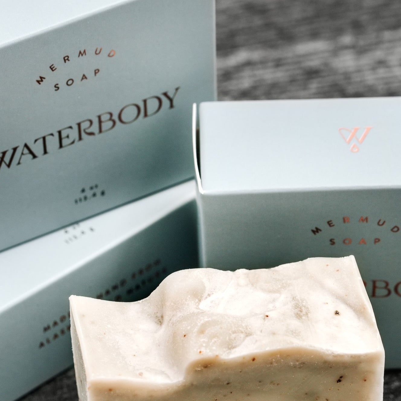A stack of soap boxes are blue and rectangle in shape. A bar of soap sits at the foreground