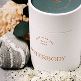 A white tube of bath soak is framed by spilled bath salts, a rock, eucalyptus leaves, and sea sponge.