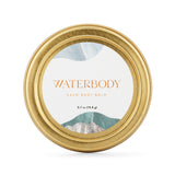 A gold tin of Waterbody Calm Body Balm is staged against a white backdrop
